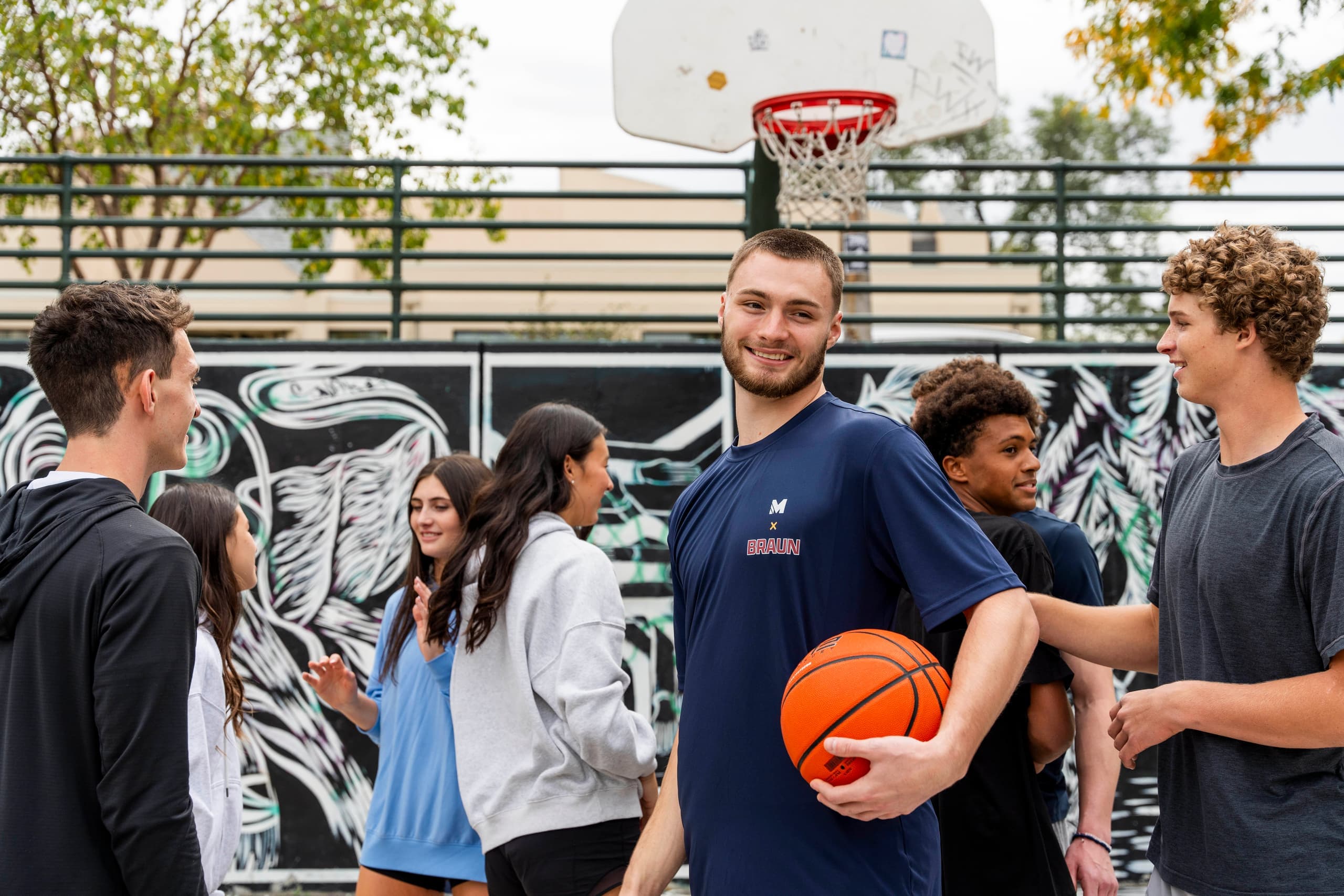 Christian Braun smiling with a basketball while standing with young people on an outdoor court.